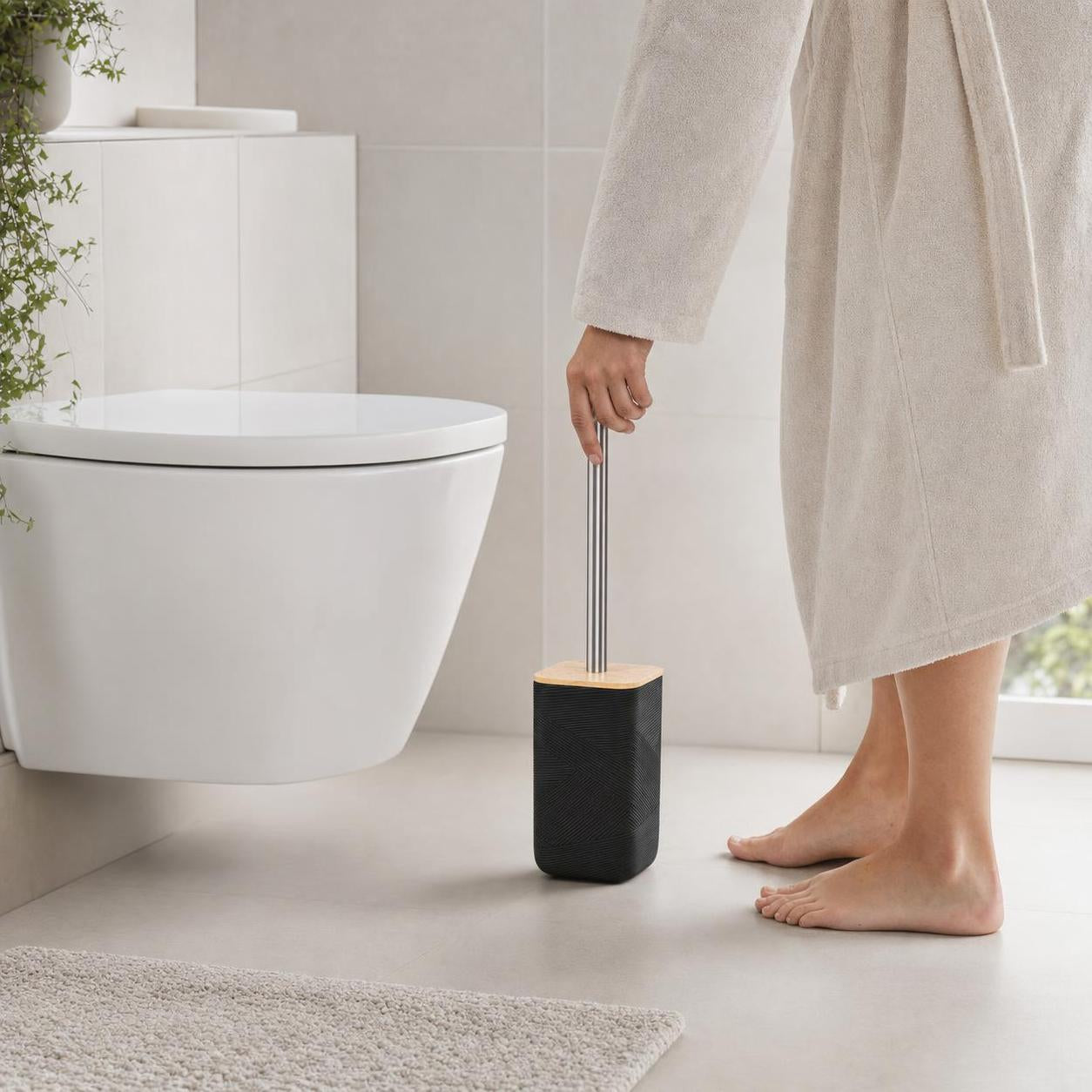 Eine schwarze WC-Bürste mit Holzdeckel steht neben der Toilette.