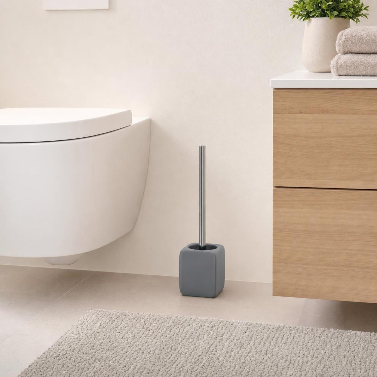 Graue WC-Bürste steht neben Toilette und Holzwaschtisch im Bad.