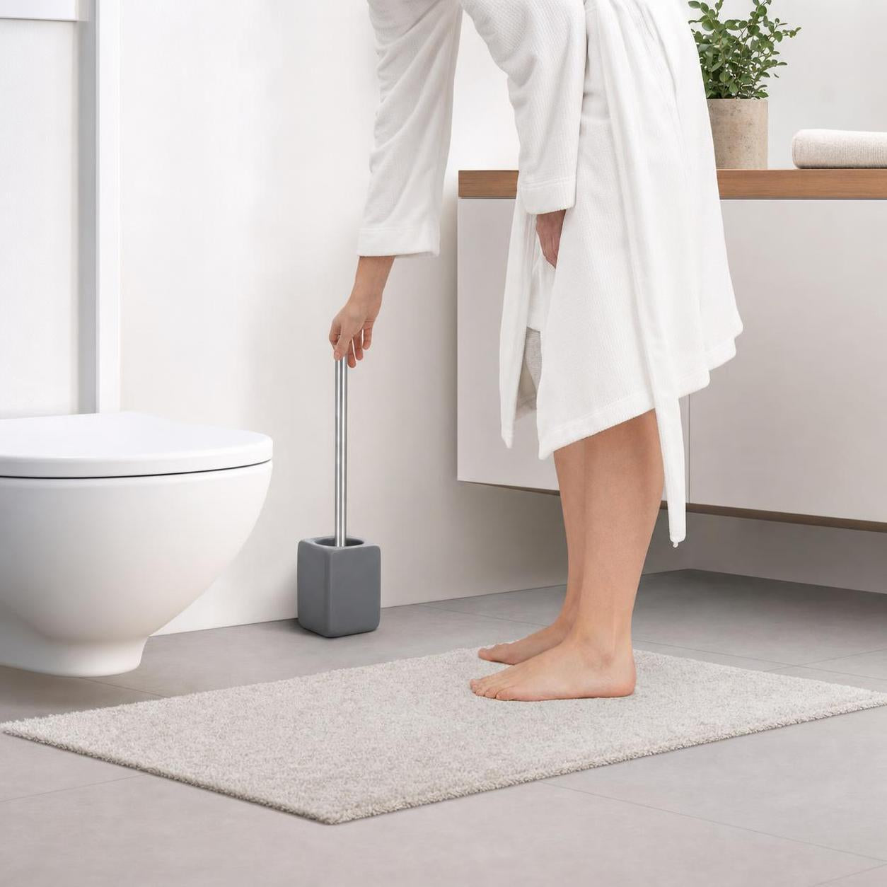 Eine graue WC-Bürste steht neben der Toilette im modernen Bad.