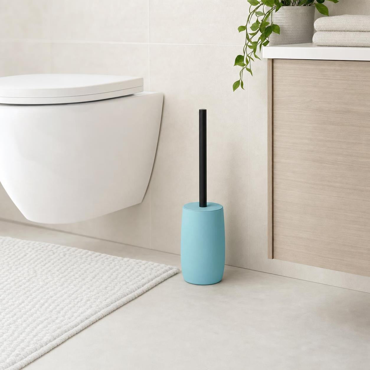 Eine blaue WC-Bürste mit schwarzem Griff steht neben der Toilette.