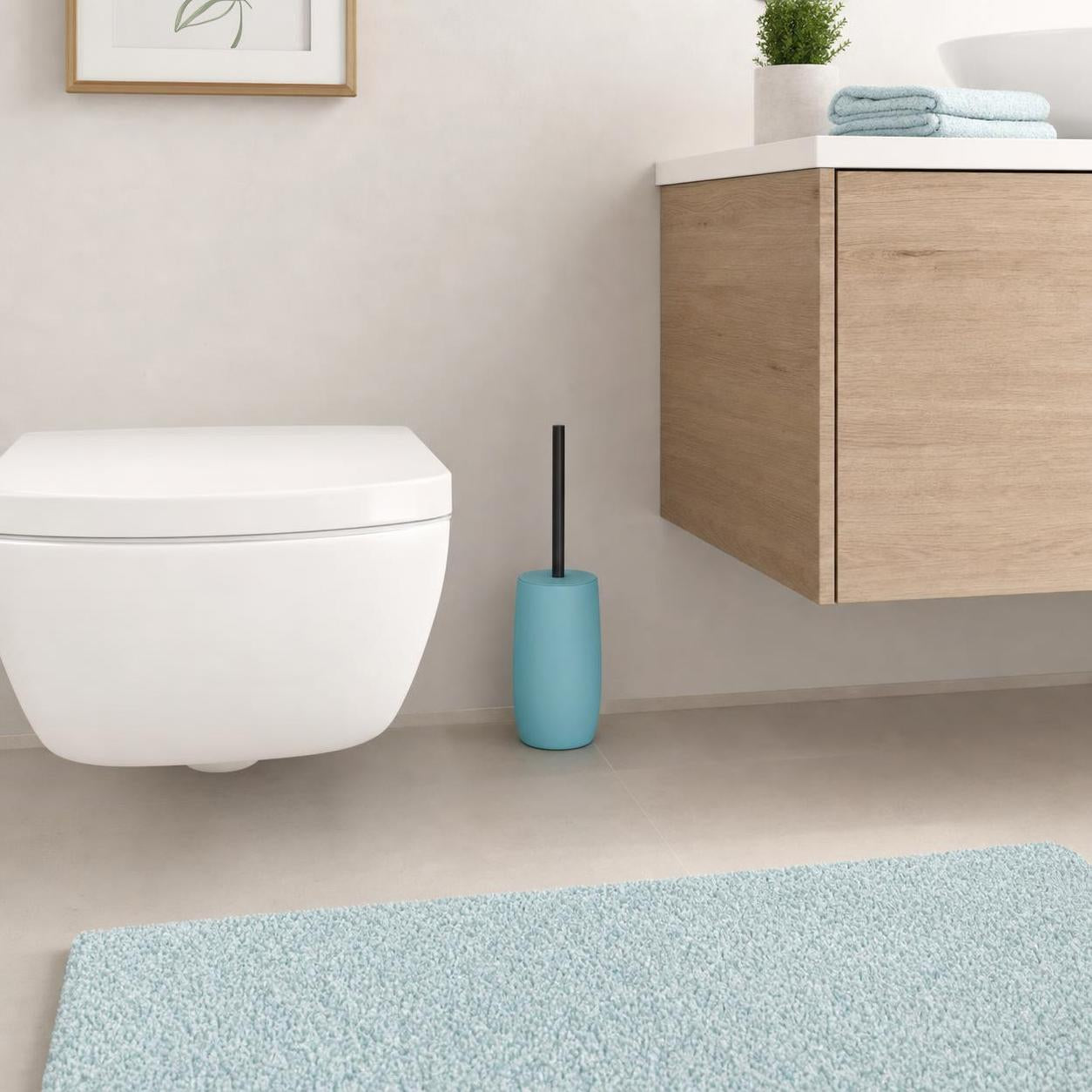 Eine türkisfarbene WC-Bürste steht neben Toilette und Holzwaschtisch.