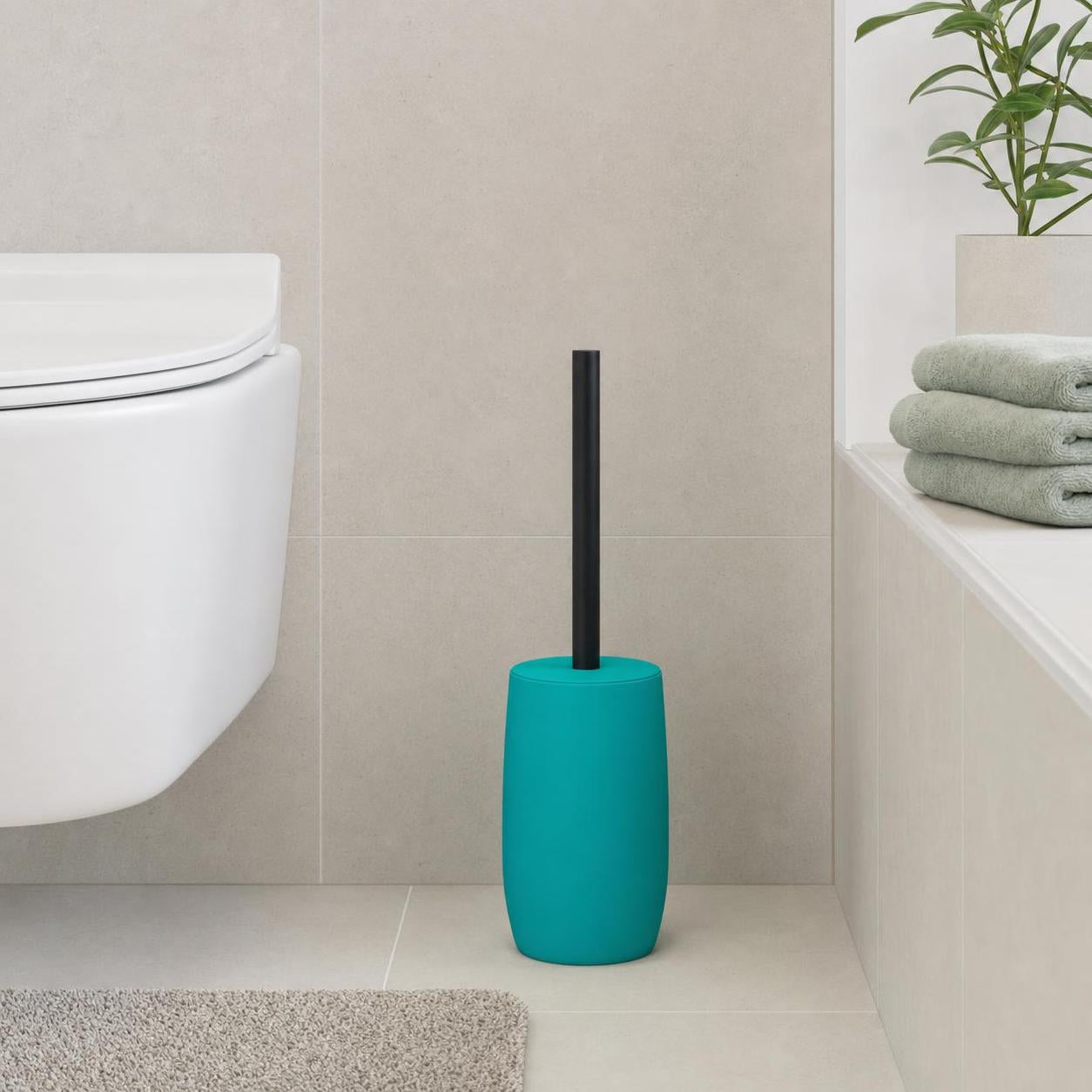 Türkise Toilettenbürste mit schwarzem Griff steht neben dem WC.
