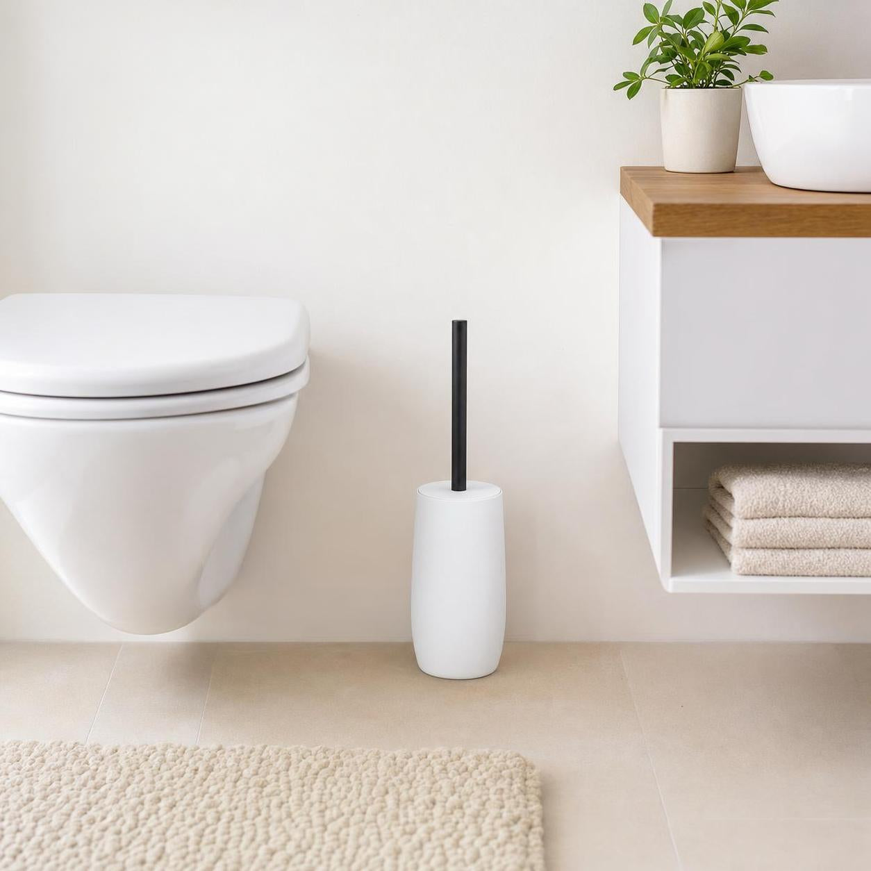 Weiße WC-Bürste mit schwarzem Griff steht neben der Toilette im Bad.