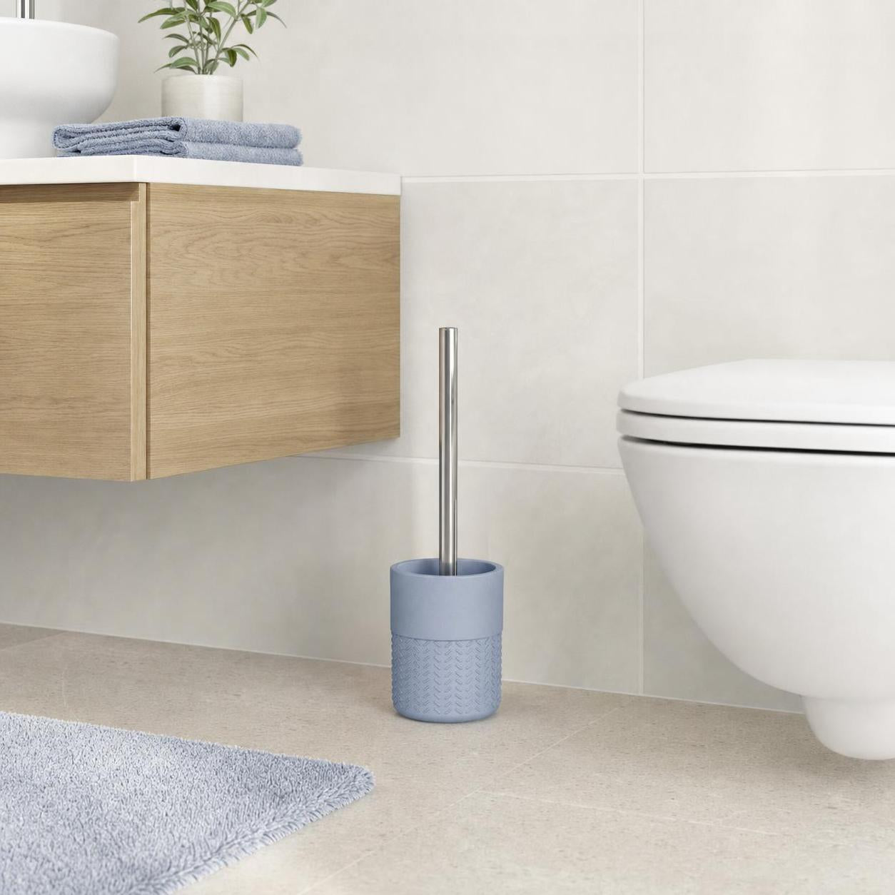 Eine blaue WC-Bürste steht neben der Toilette im hellen Bad.