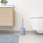 Eine hellblaue WC-Bürste steht neben der Toilette im hellen Bad.