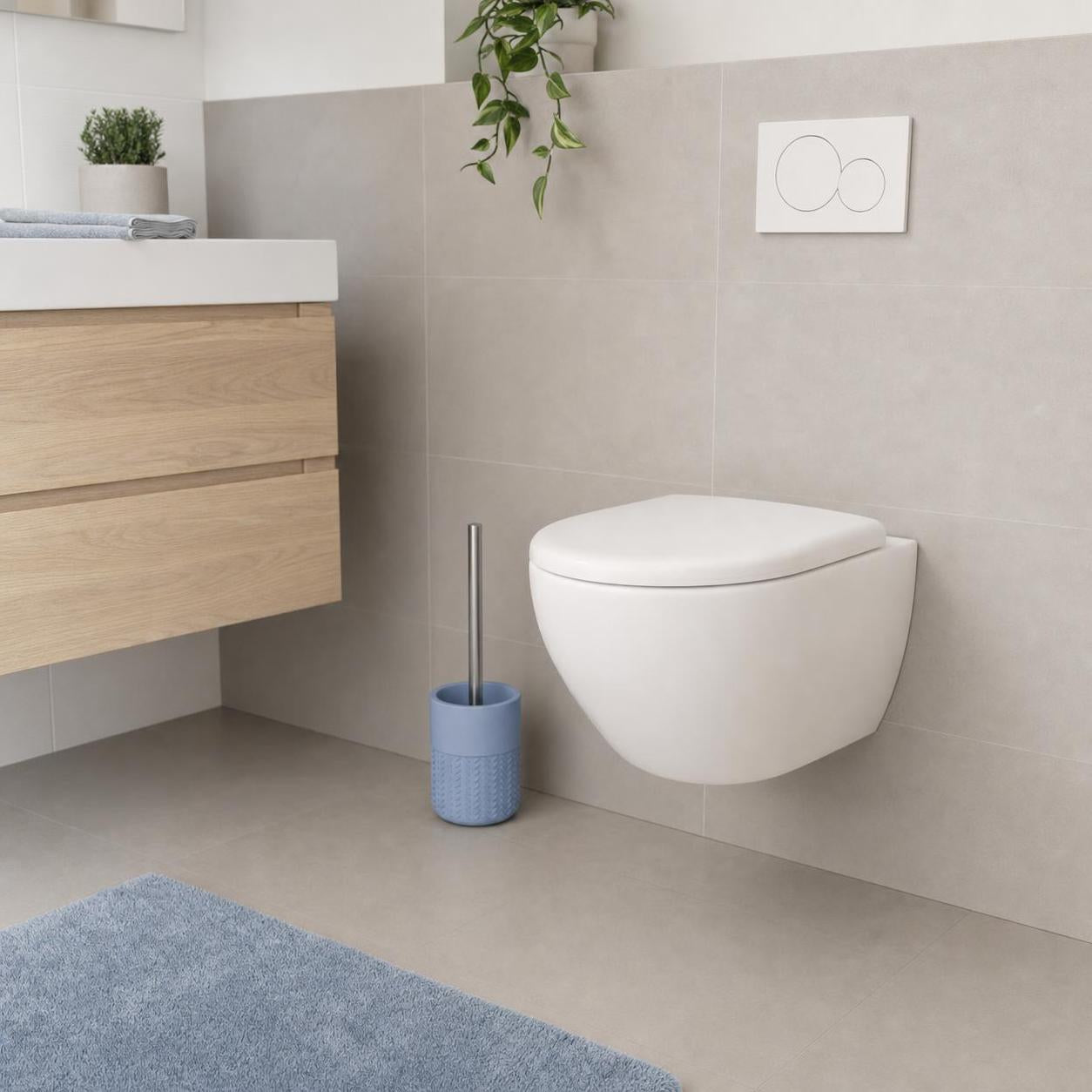 Blaue WC-Bürste steht neben einer wandhängenden Toilette im Bad.