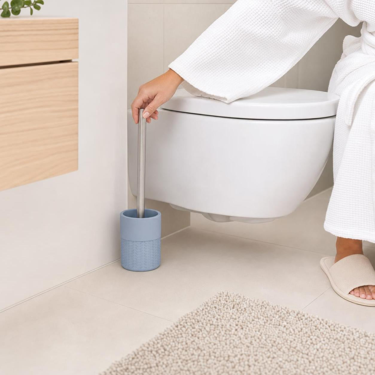 Eine Hand greift die blaue Toilettenbürste neben dem WC.