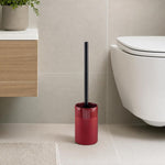 Eine rote WC-Bürste mit schwarzem Griff steht neben der Toilette.