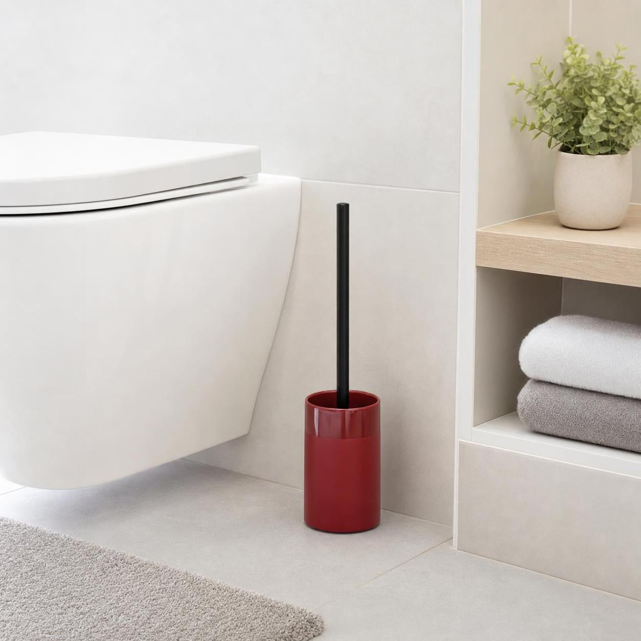 Rote WC-Bürste mit schwarzem Griff steht neben der Toilette im Bad.
