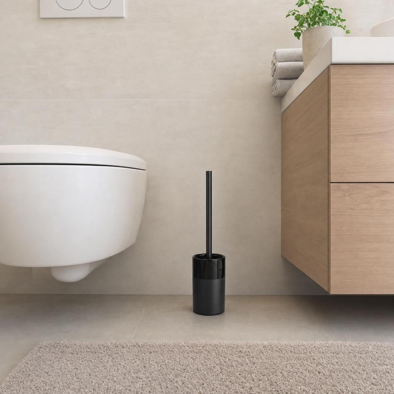 Schwarze WC-Bürste in modernem Badezimmer neben Wand-WC und Waschtisch.