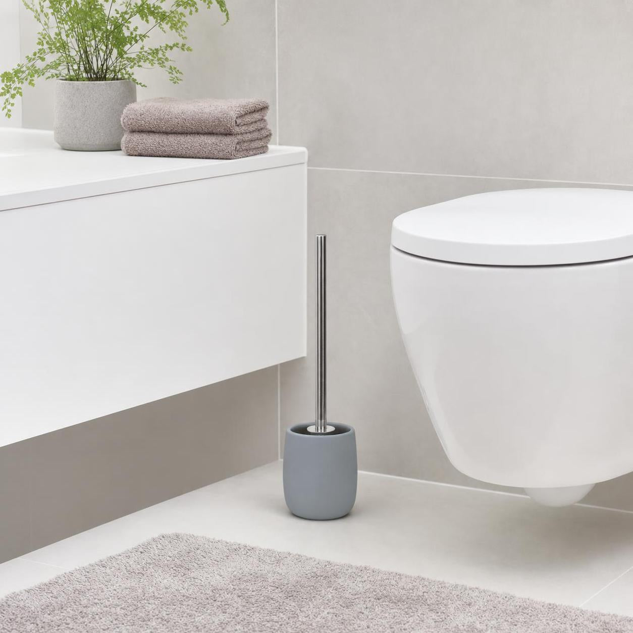Graue WC-Bürste steht neben einer weißen Toilette im modernen Bad.