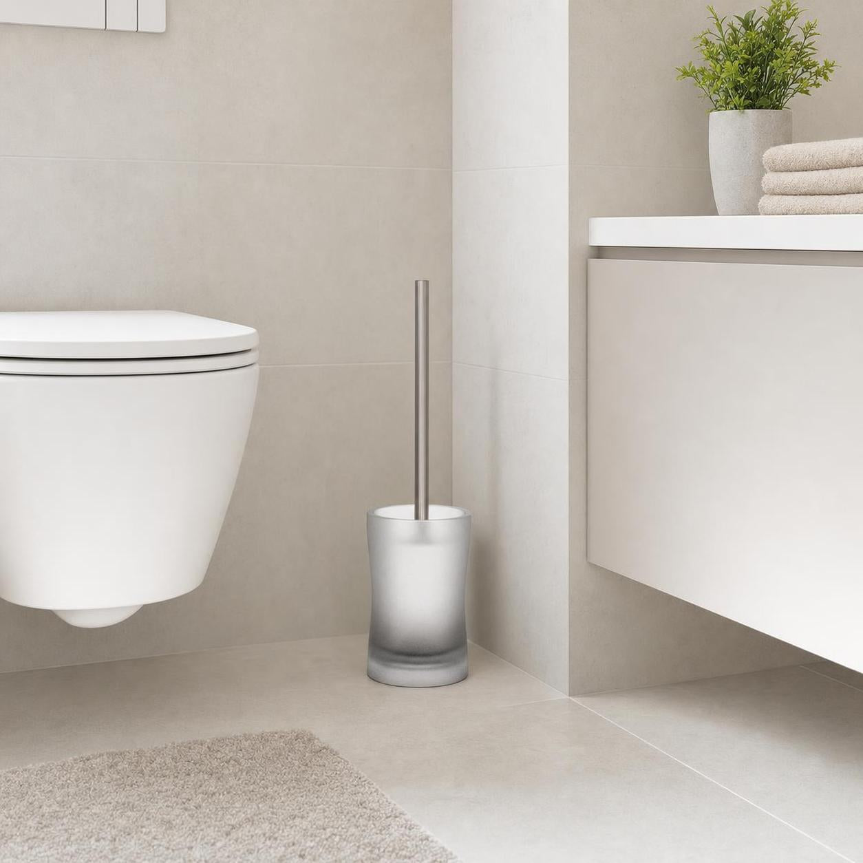 Eine WC-Bürste mit Milchglasbehälter steht neben der Toilette.