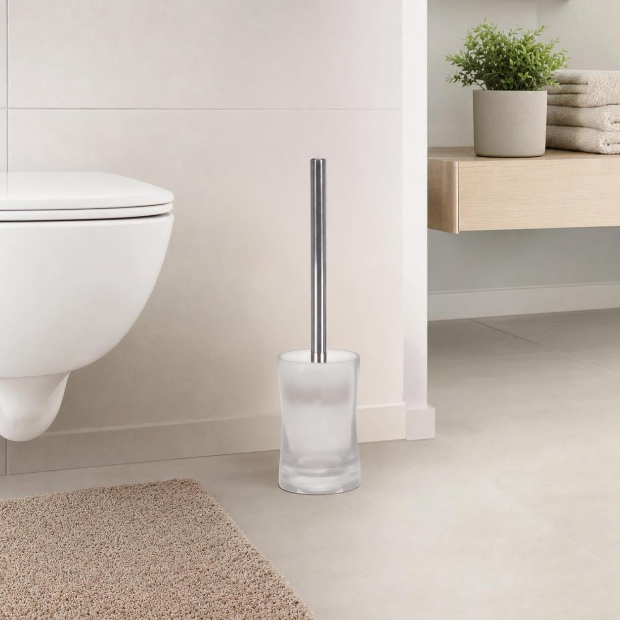 Eine WC-Bürste im satinierten Glasbehälter steht neben der Toilette.