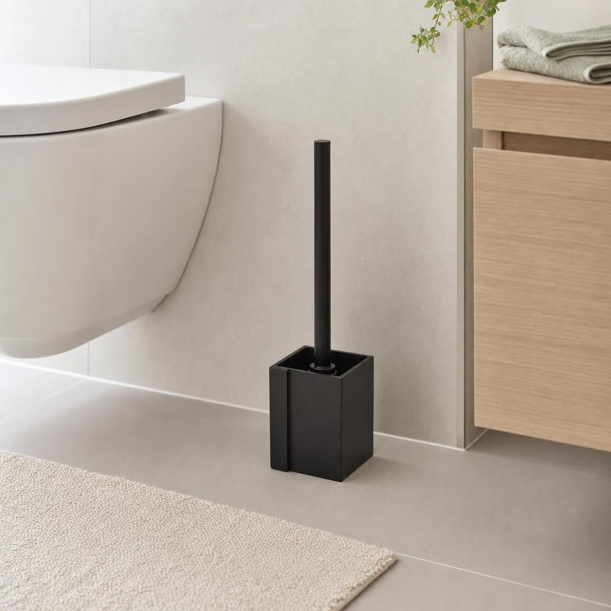 Schwarze WC-Bürste steht neben Toilette und Holzschrank im Bad.