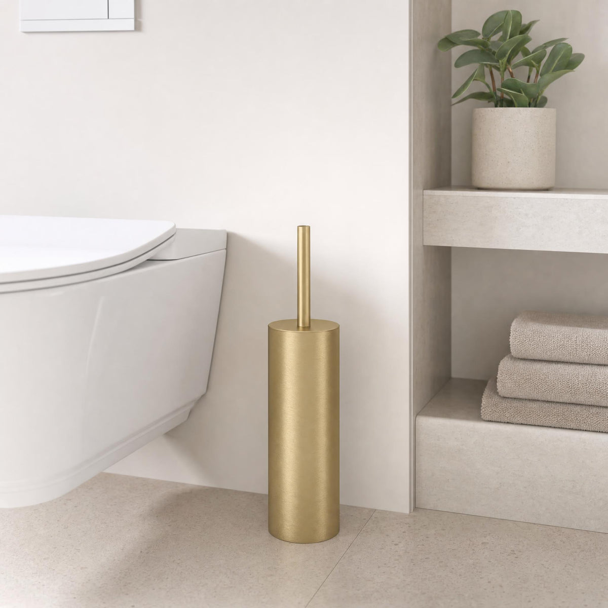 Goldfarbene WC-Bürste neben Wand-WC in modernem Bad mit Regal und Pflanze.