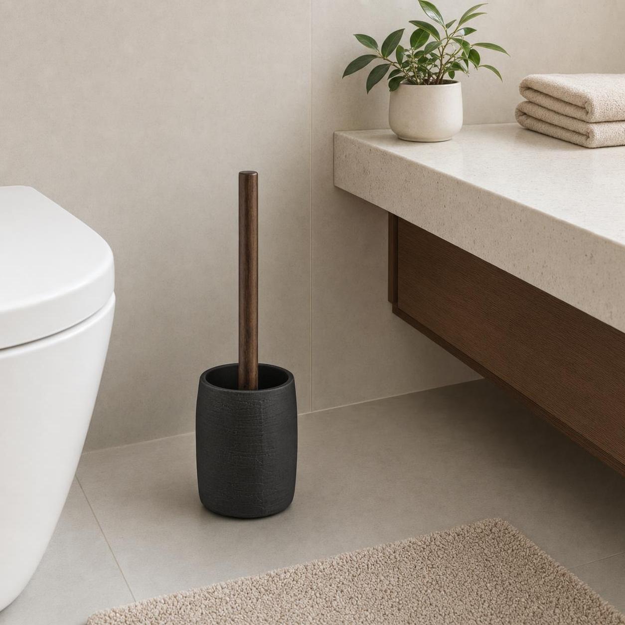 Eine WC-Bürste mit Holzgriff steht im schwarzen Halter neben der Toilette.
