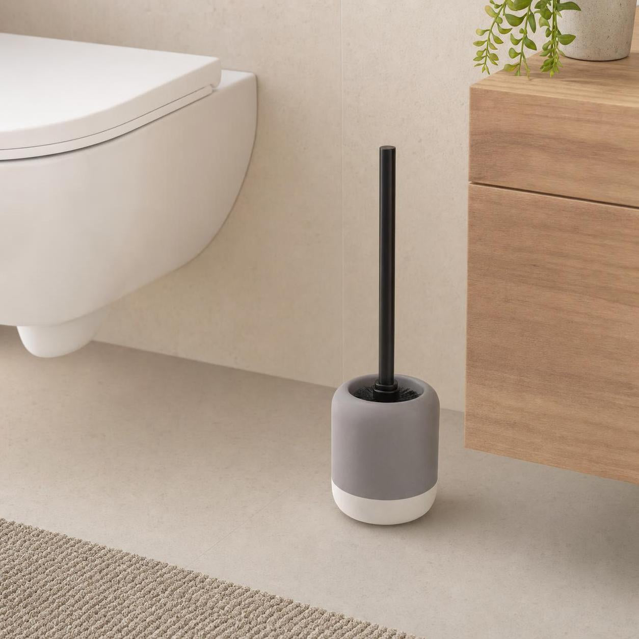 Graue WC-Bürste mit schwarzem Griff steht neben Toilette und Holzschrank.