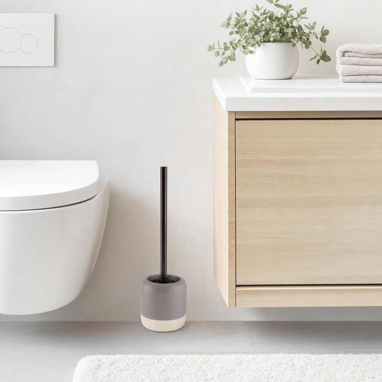 Graue WC-Bürste mit schwarzem Griff steht neben Toilette und Waschtisch.