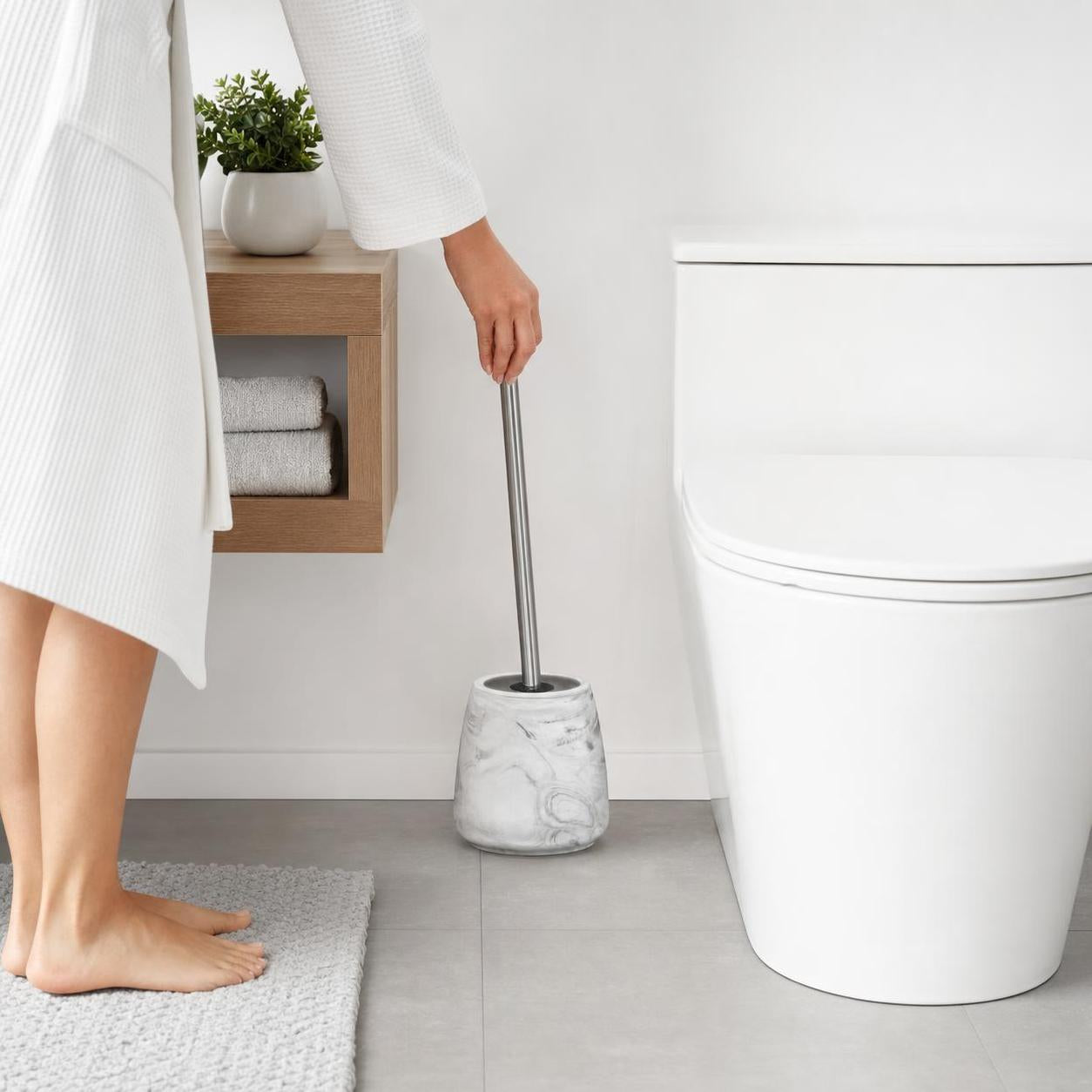 Eine WC-Bürste mit marmoriertem Halter steht im hellen Bad.