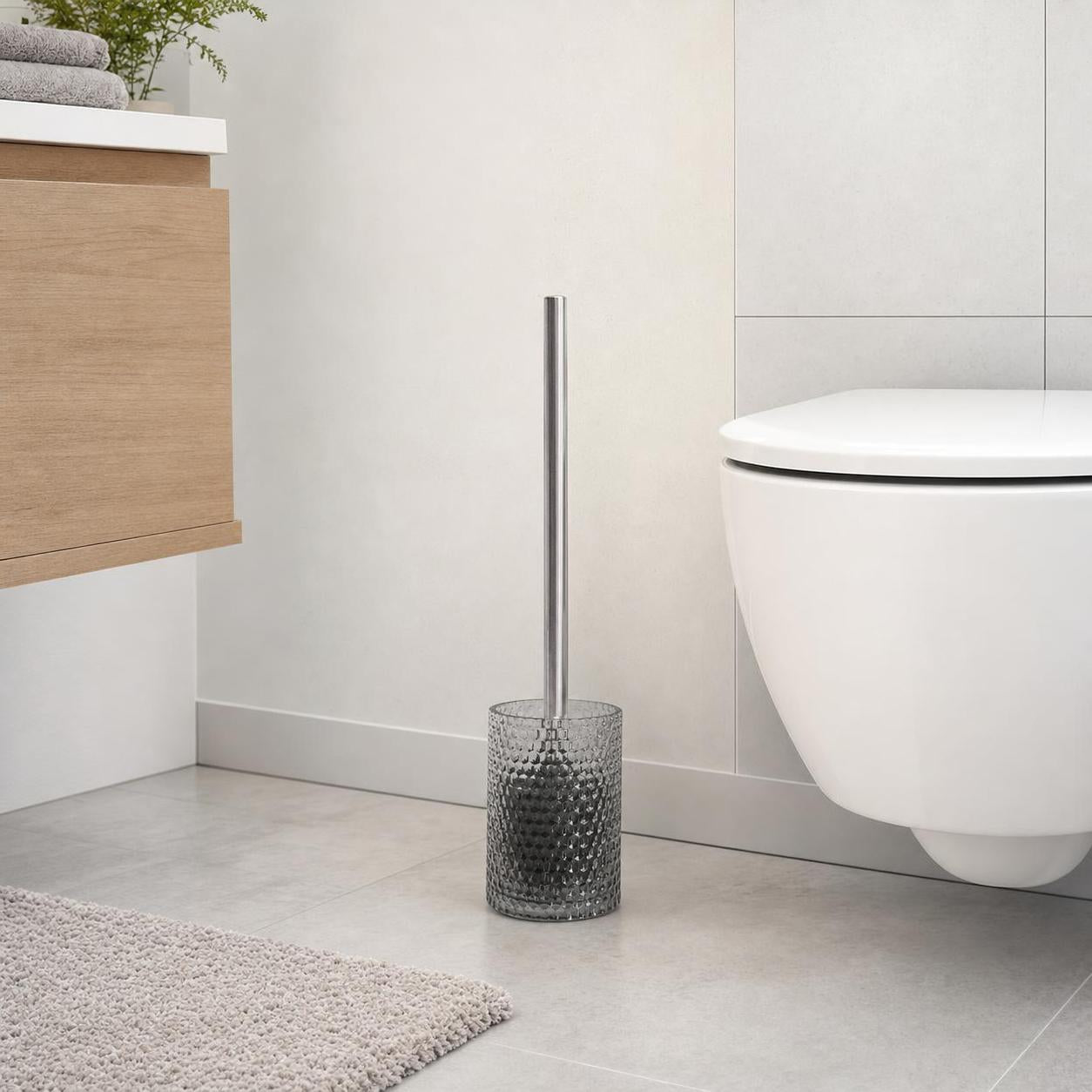 WC-Bürste im strukturierten Glasbehälter steht neben der Toilette.