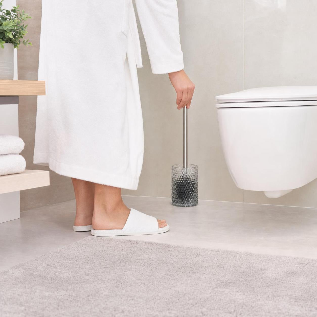 Eine WC-Bürste mit grauem Glasbehälter steht neben der Toilette.