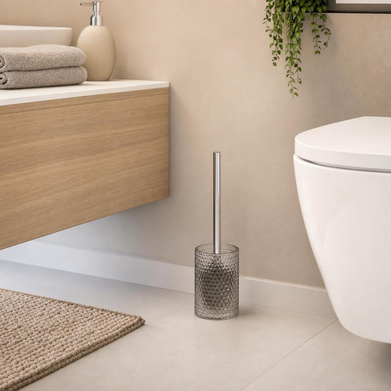 Eine WC-Bürste im strukturierten Glasbehälter steht neben der Toilette.