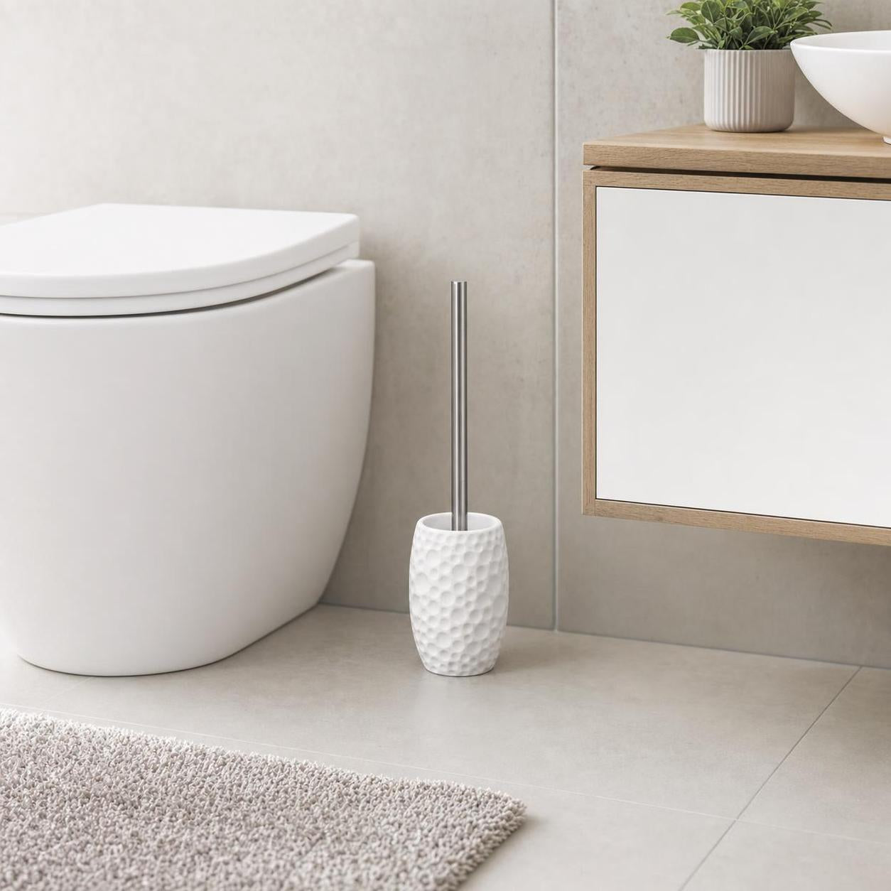 Weiße WC-Bürste mit strukturierter Halterung steht neben der Toilette.