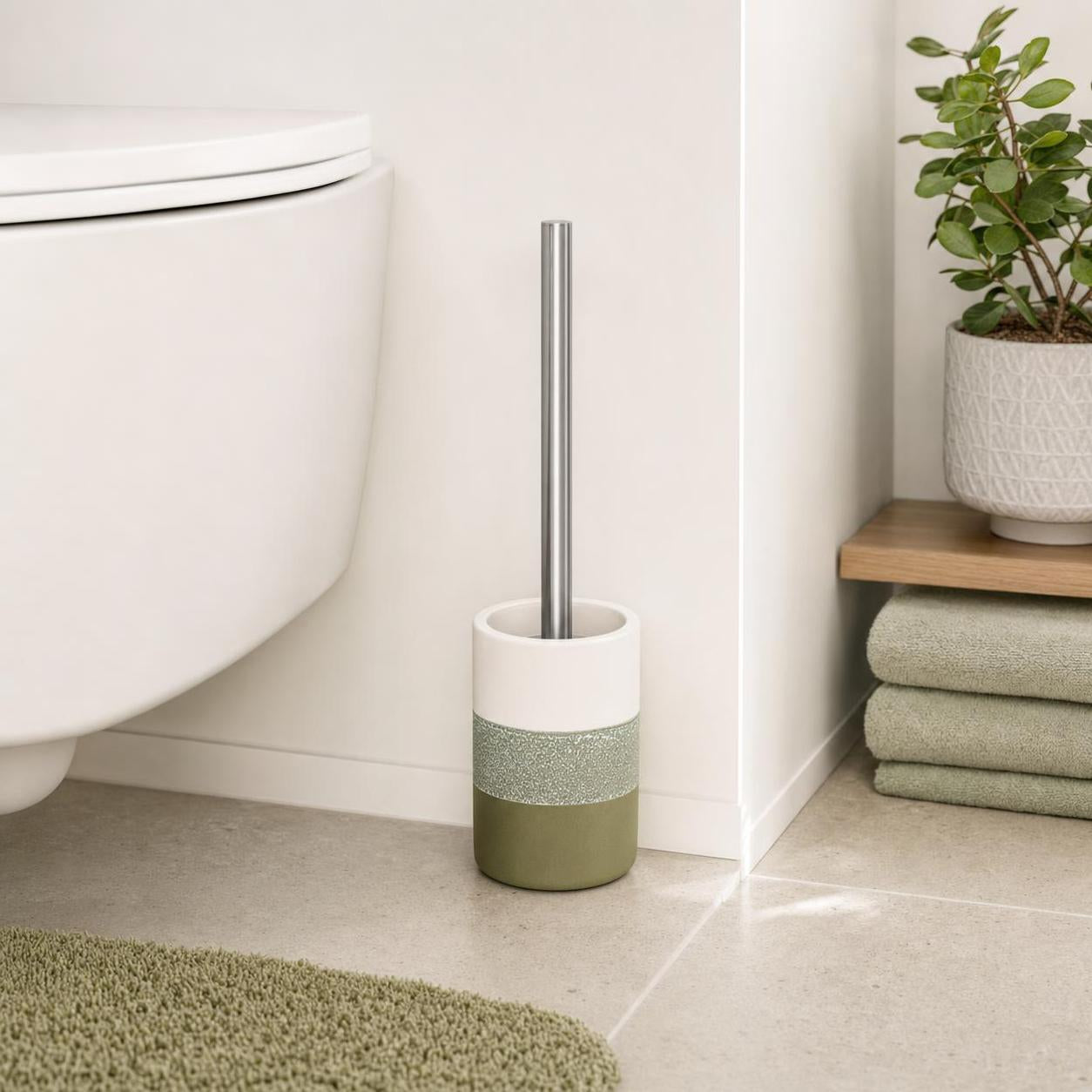 Eine WC-Bürste in grün-weißem Halter steht neben der Toilette.