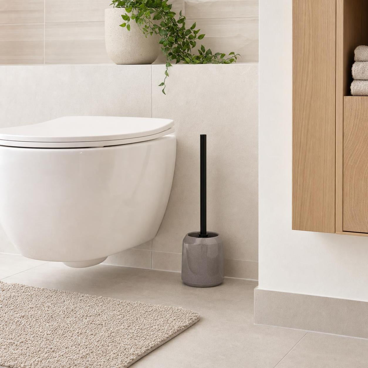 Graue WC-Bürste steht neben einer weißen Toilette im modernen Bad.