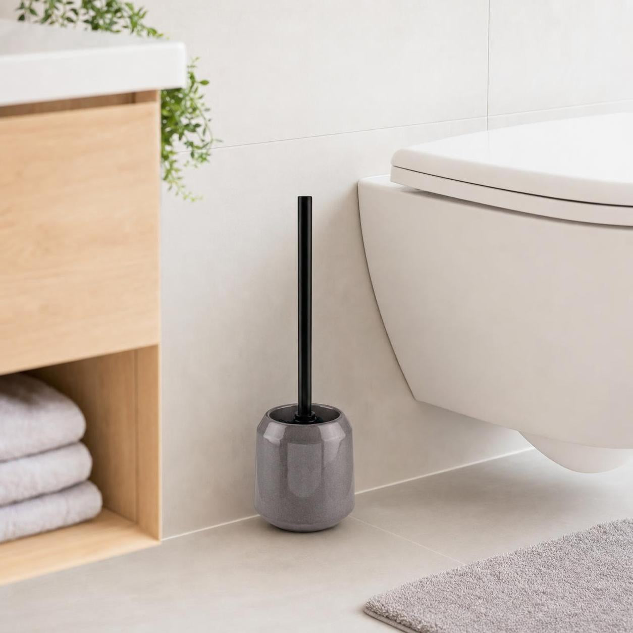 Graue WC-Bürste mit schwarzem Griff steht neben der Toilette.