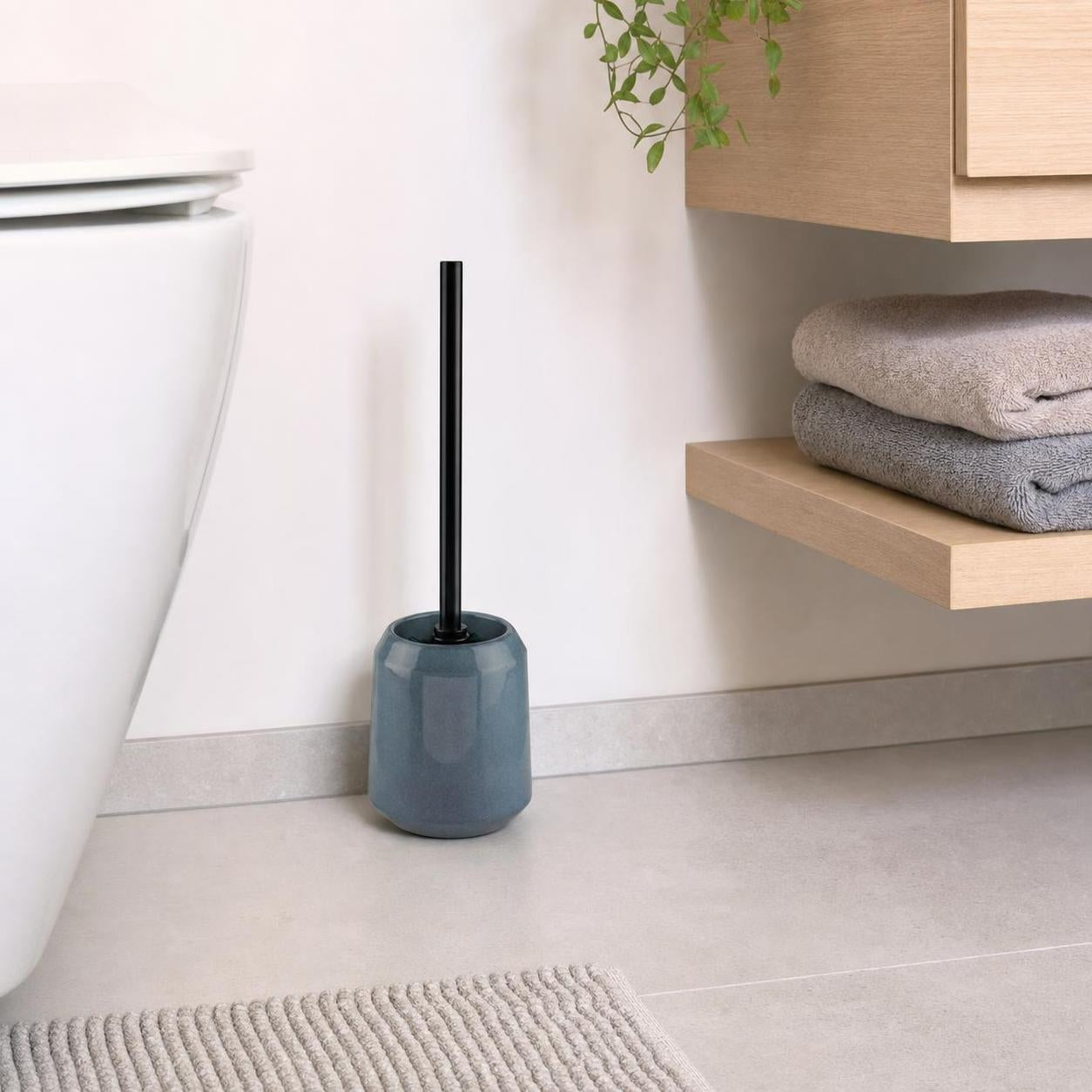 Eine WC-Bürste im blauen Halter steht neben der Toilette.