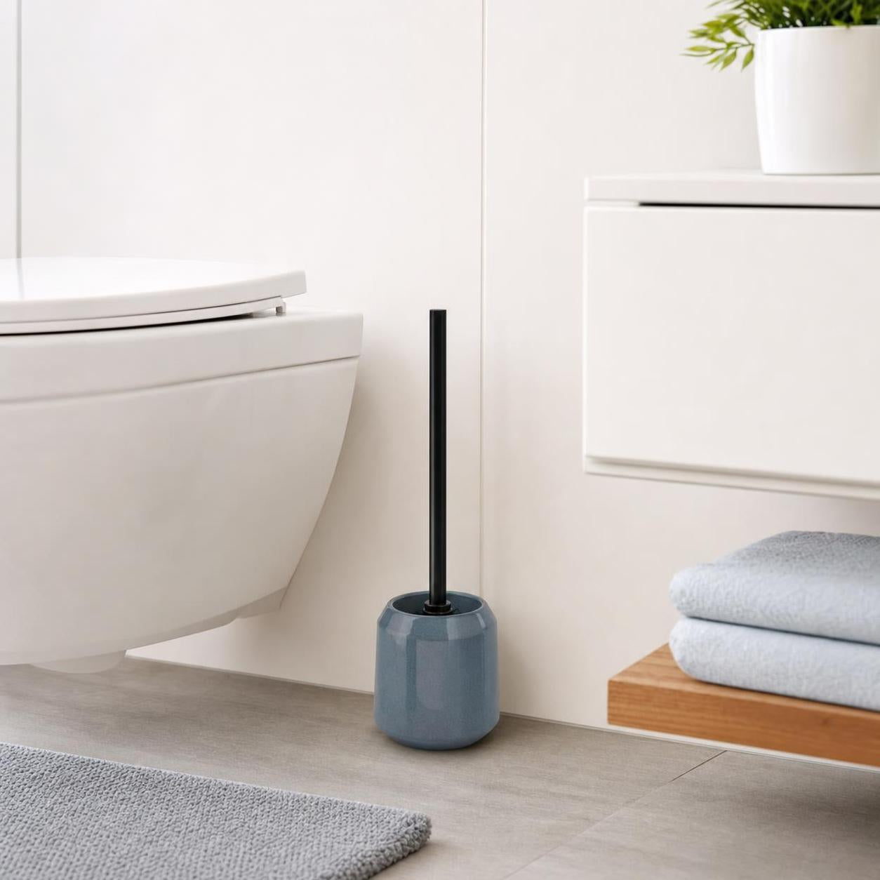 Eine blaue Toilettenbürste steht neben der Toilette im hellen Bad.