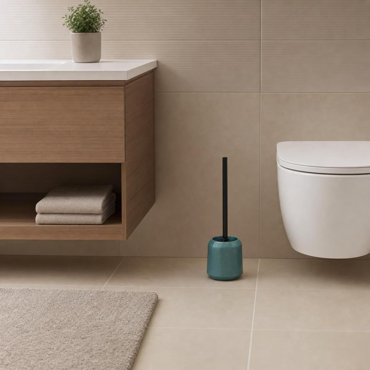 Türkise WC-Bürste mit schwarzem Griff steht neben der Toilette.