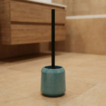 Türkisfarbener WC-Bürstenhalter mit schwarzem Stiel auf Fliesenboden