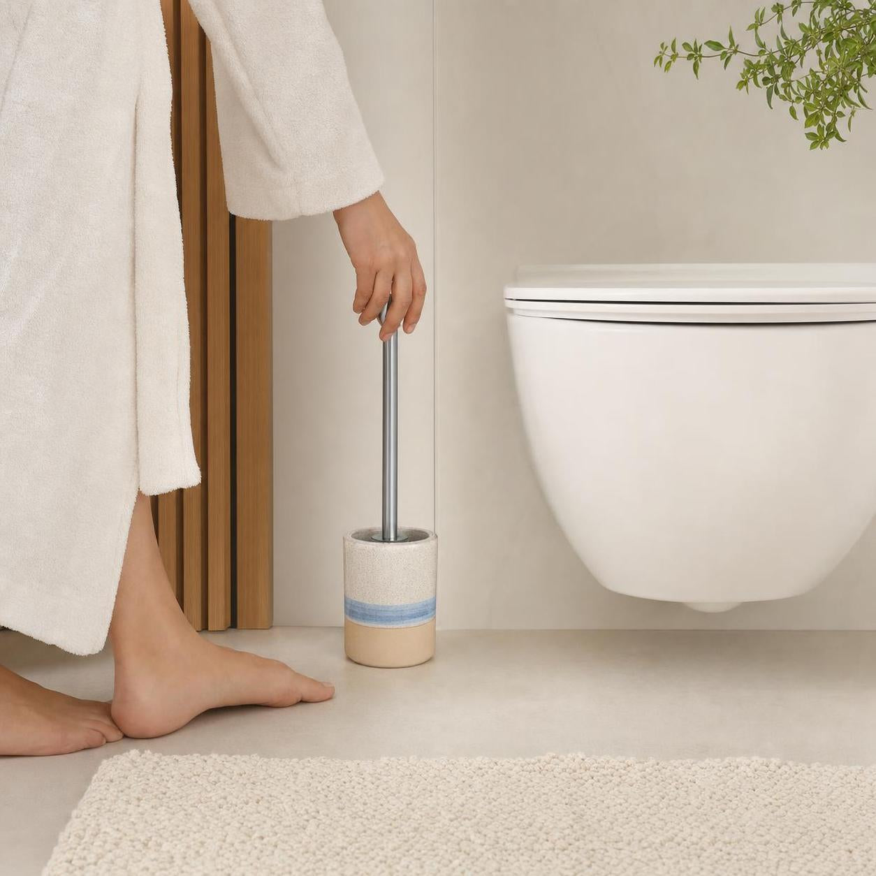 Eine WC-Bürste im beigen Halter mit blauem Streifen steht neben dem WC.
