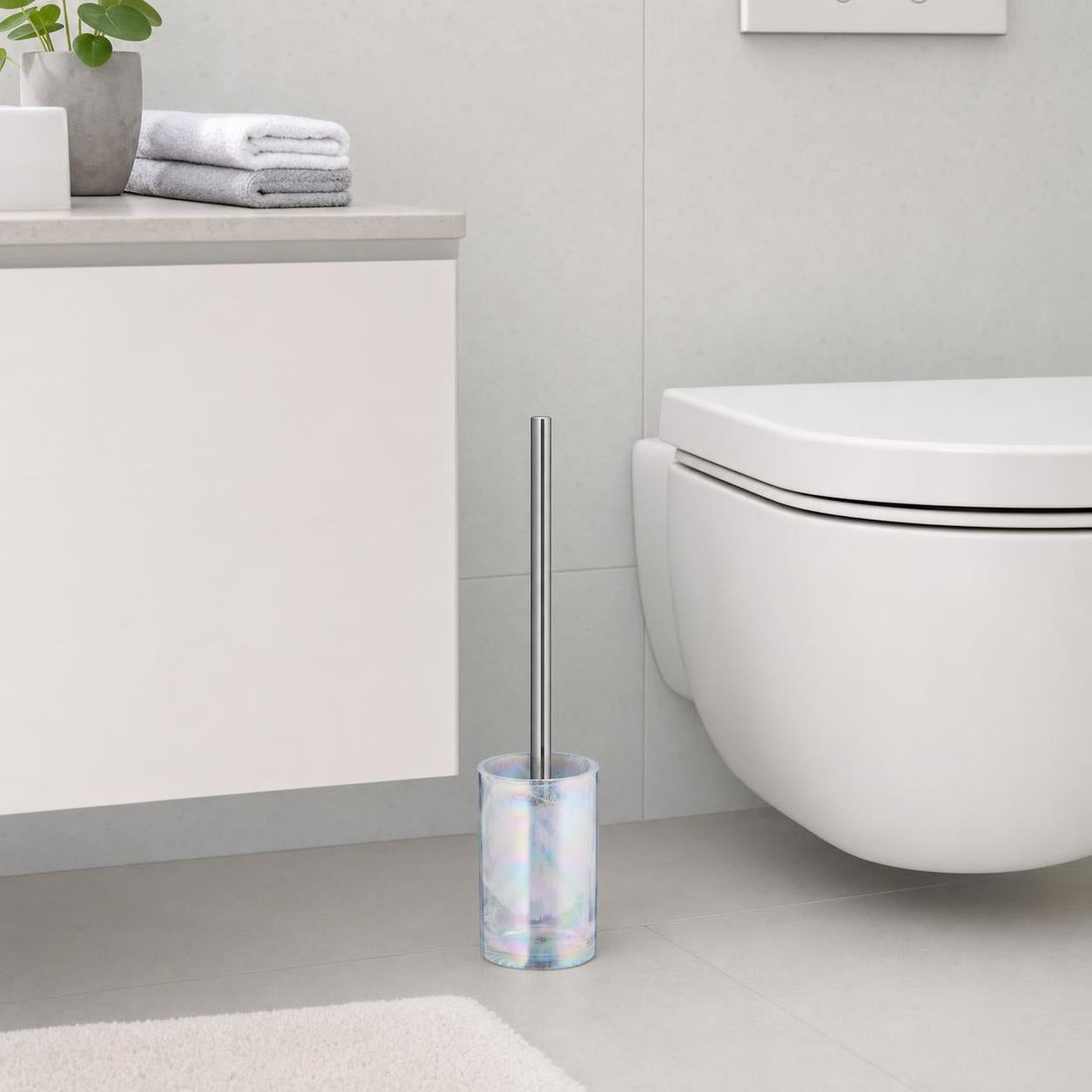 Eine WC-Bürste mit schimmerndem Halter steht neben der Toilette.