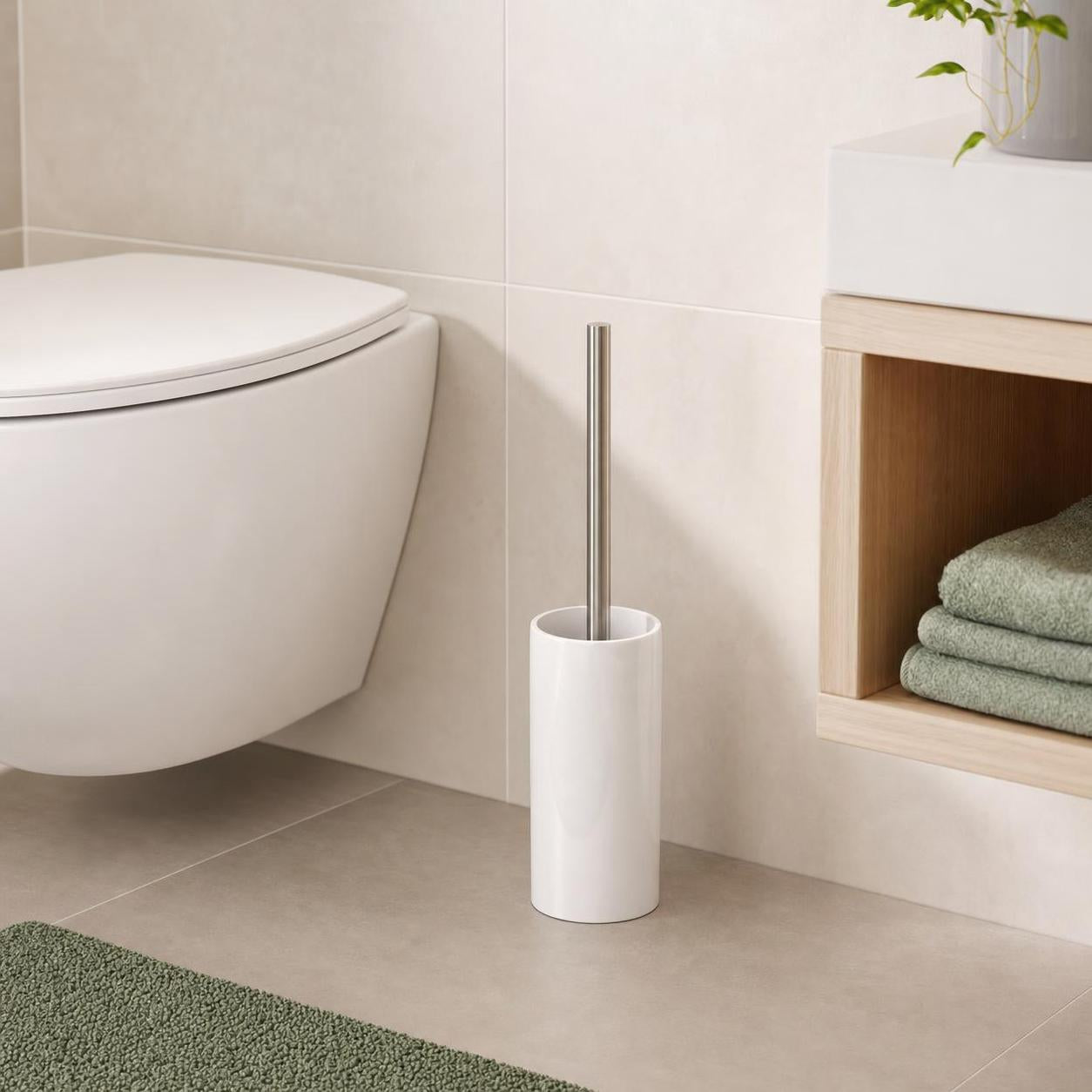 Weiße WC-Bürste mit Edelstahlgriff steht neben der Toilette im Bad.