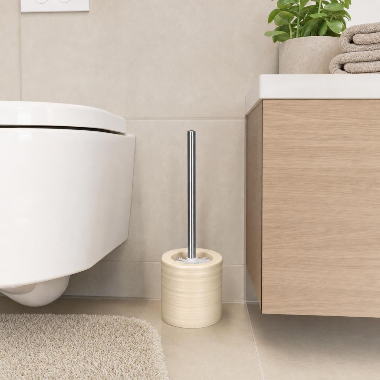 Eine WC-Bürste mit beigefarbenem Halter steht neben der Toilette.