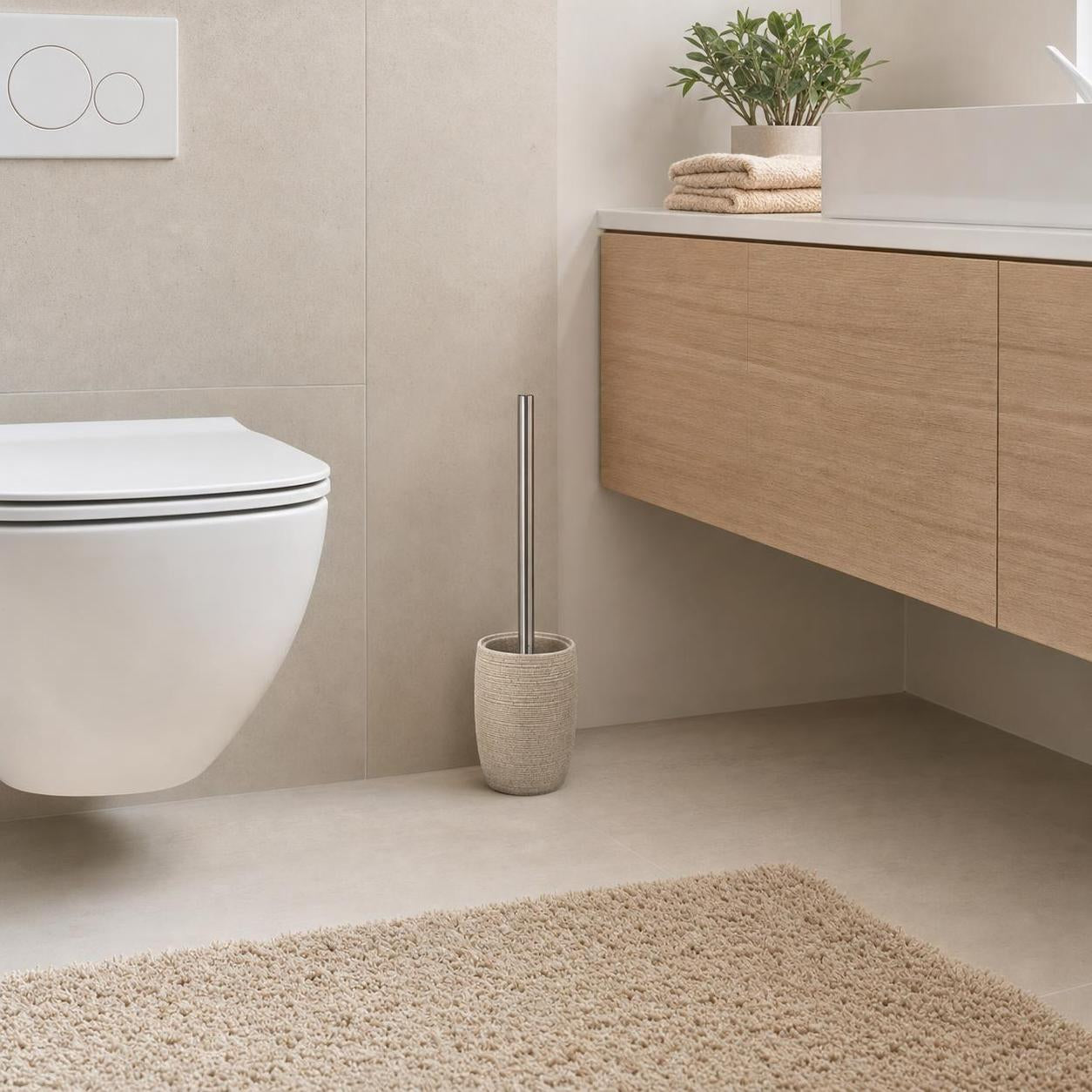 Eine WC-Bürste im beigen Halter steht neben Toilette und Waschtisch.