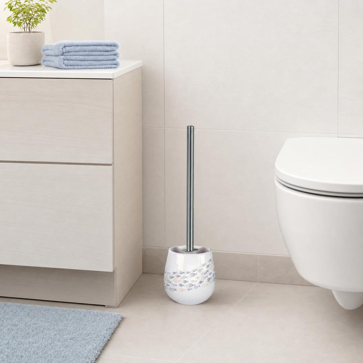Weiße WC-Bürste mit Fischmotiv steht neben der Toilette im Bad.