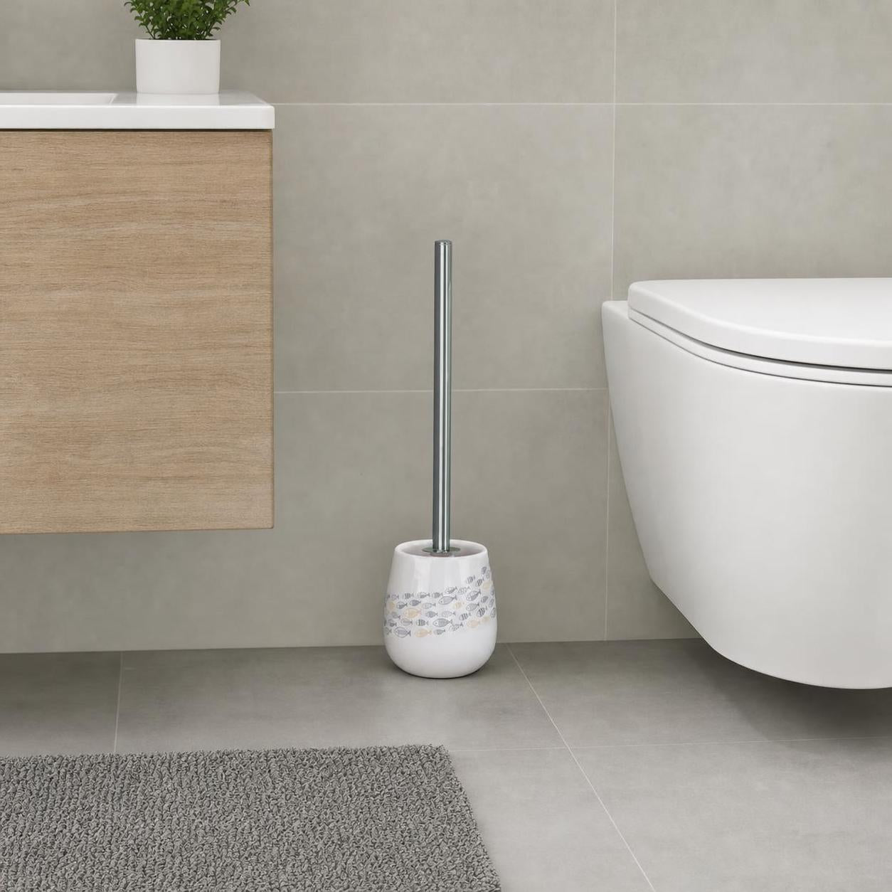 Weiße WC-Bürste mit Fischmuster steht neben der Toilette im Bad.
