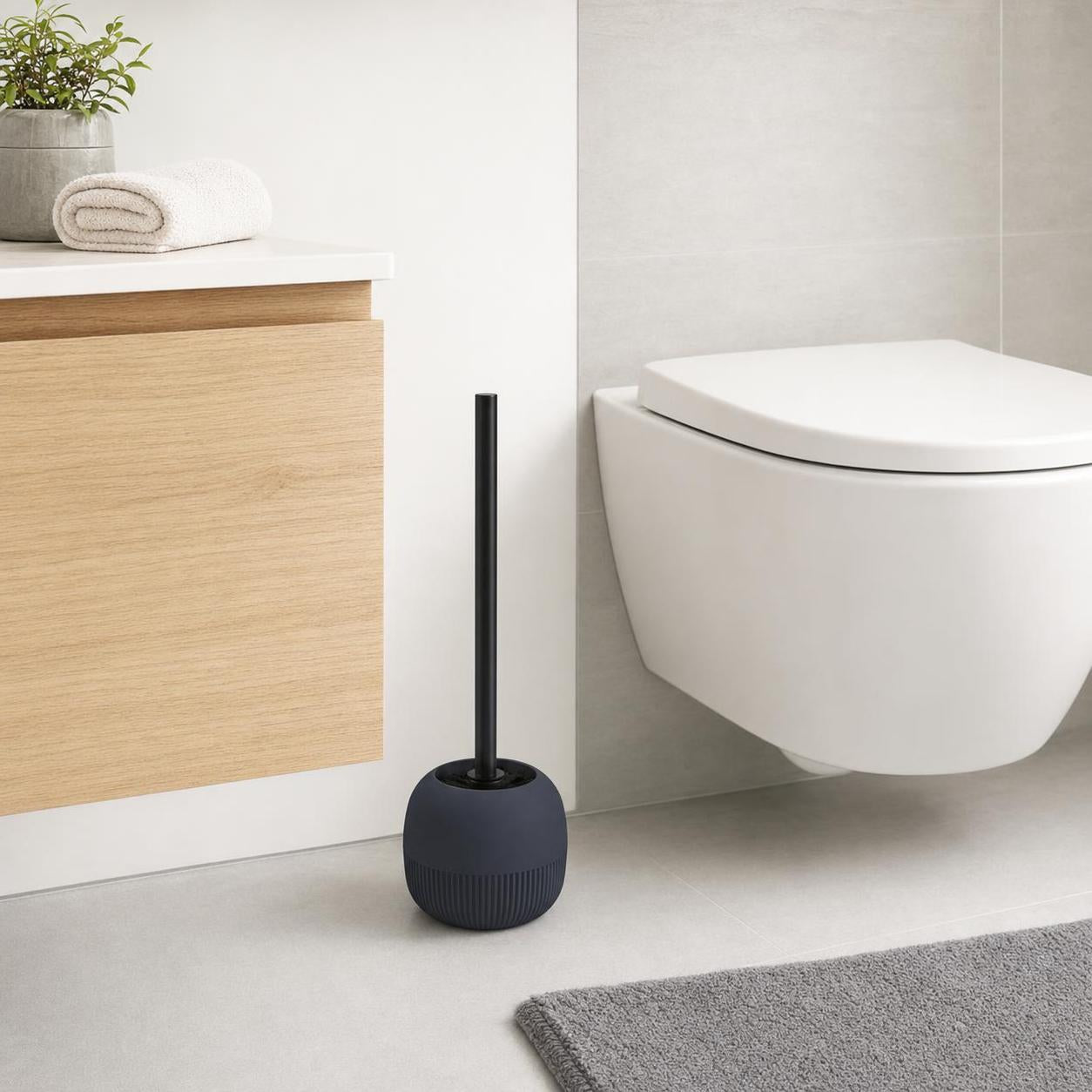 Dunkle WC-Bürste im Halter steht neben einer Toilette im Bad.