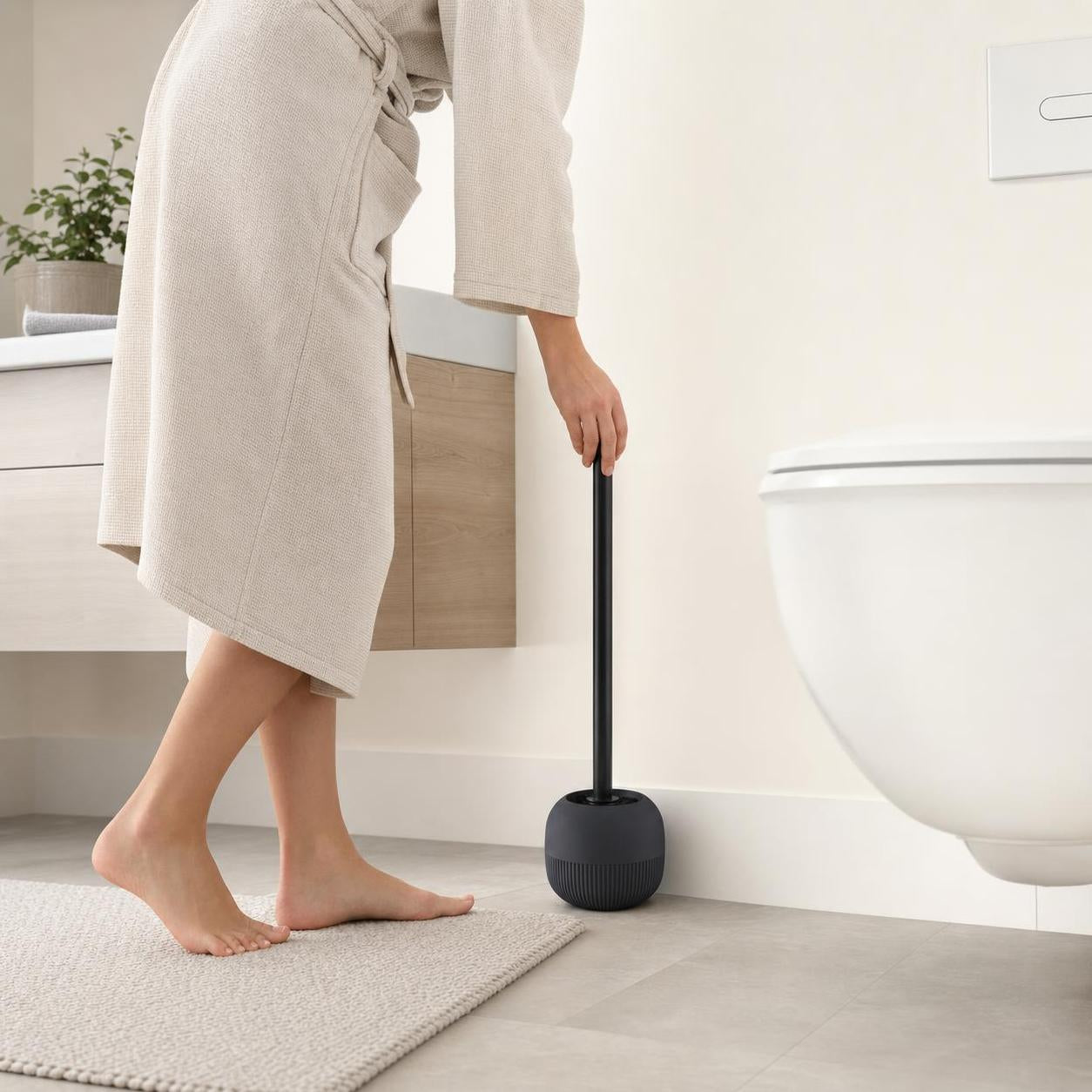 Eine schwarze WC-Bürste steht neben der Toilette im hellen Bad.
