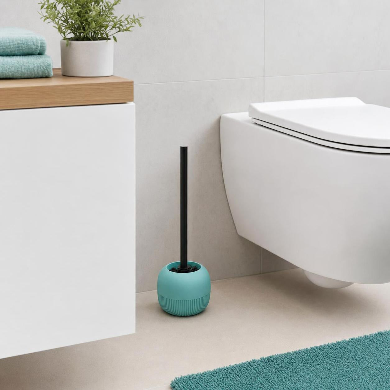 Türkise WC-Bürste mit schwarzem Griff steht neben der Toilette.