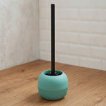 Mintgrüne WC-Bürste mit schwarzem Stiel auf Holzfußboden im Bad