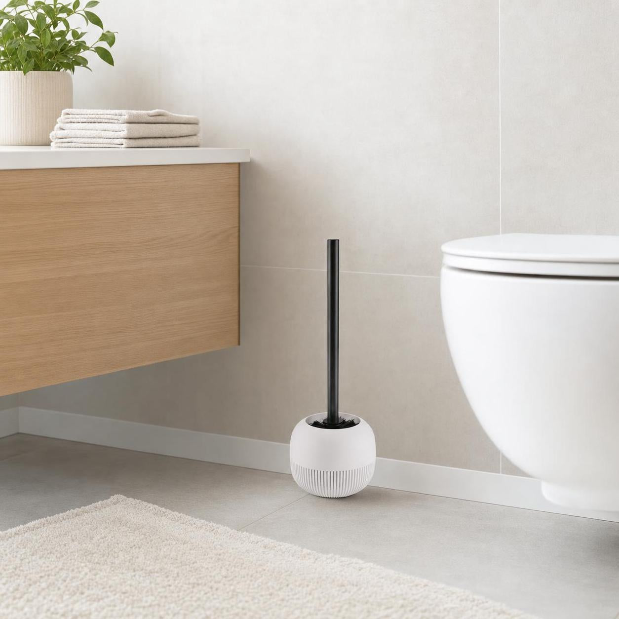 Weiße Toilettenbürste mit schwarzem Griff steht neben dem WC.