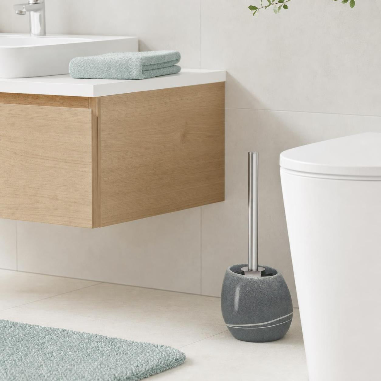 Graue WC-Bürste steht neben der Toilette in einem hellen Badezimmer.