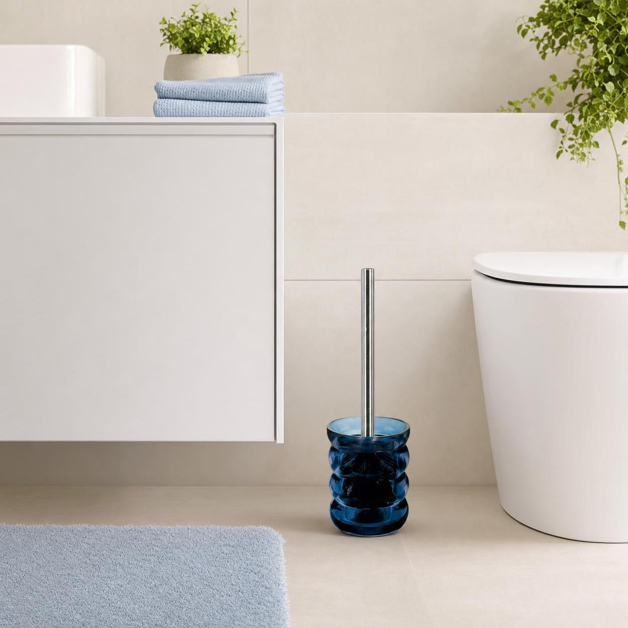 Eine blaue WC-Bürste steht neben der Toilette im hellen Bad.