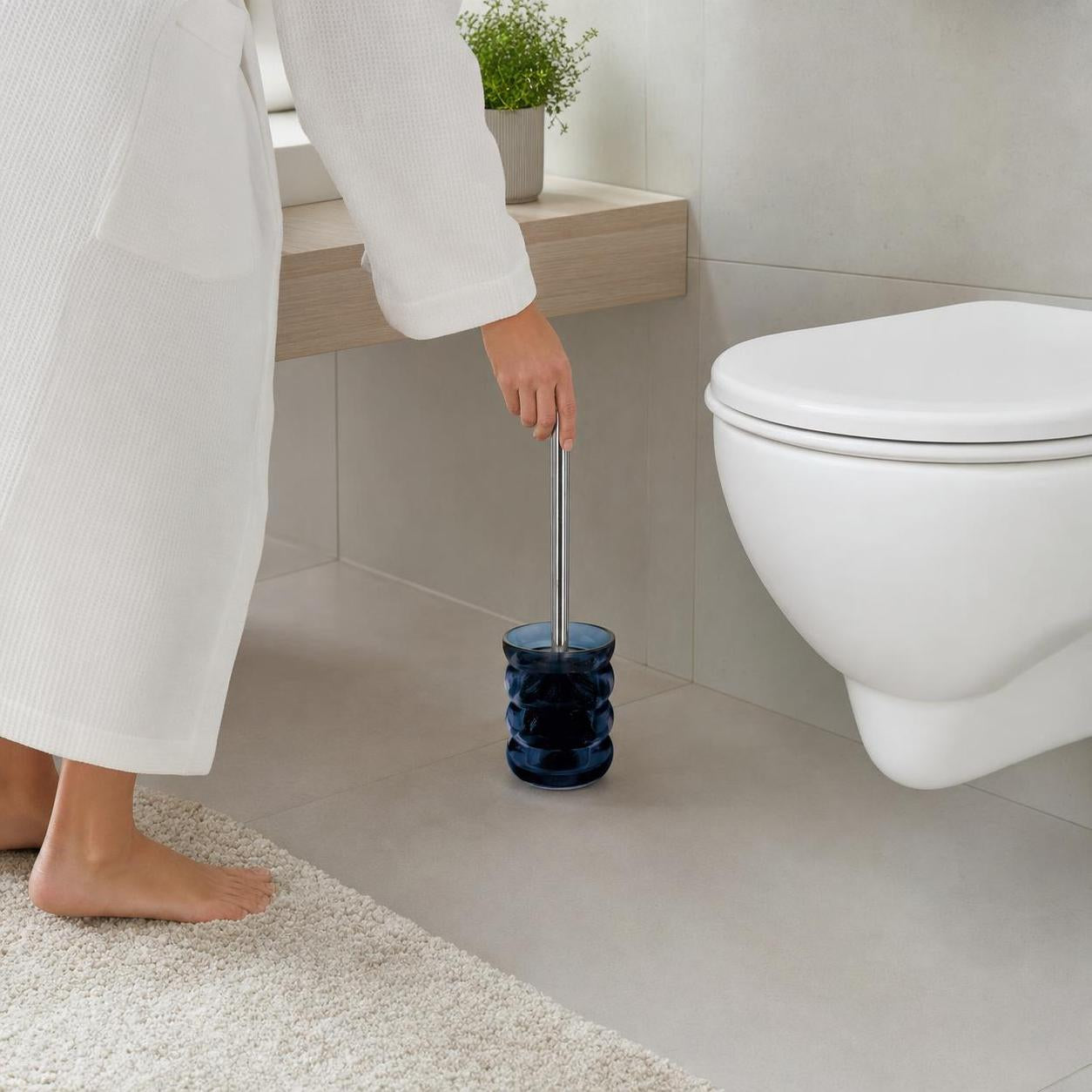 Eine Hand greift zur WC-Bürste im blauen Halter neben der Toilette.