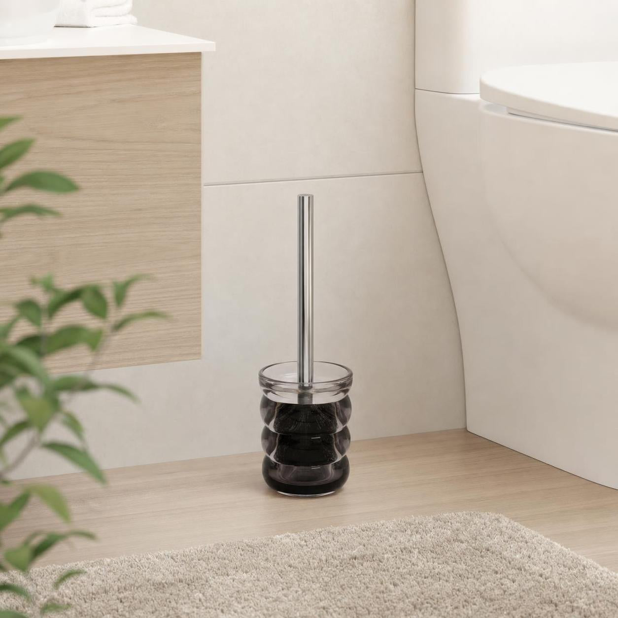 Eine WC-Bürste mit schwarzem Glasbehälter steht neben der Toilette.